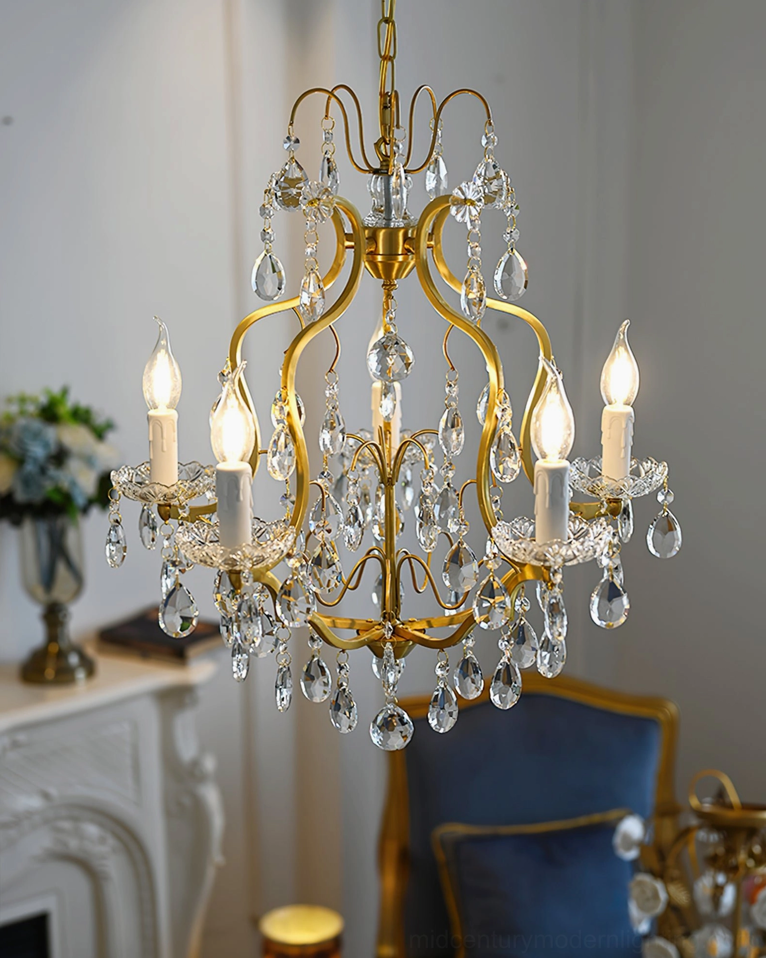 Five-head brass crystal chandelier glowing in living room with fireplace and warm ambient lighting