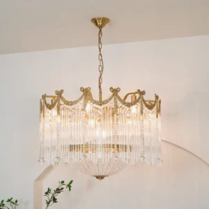 Illuminated brass crystal chandelier installed indoors with lit bulbs and cascading glass pendants against white arched wall
