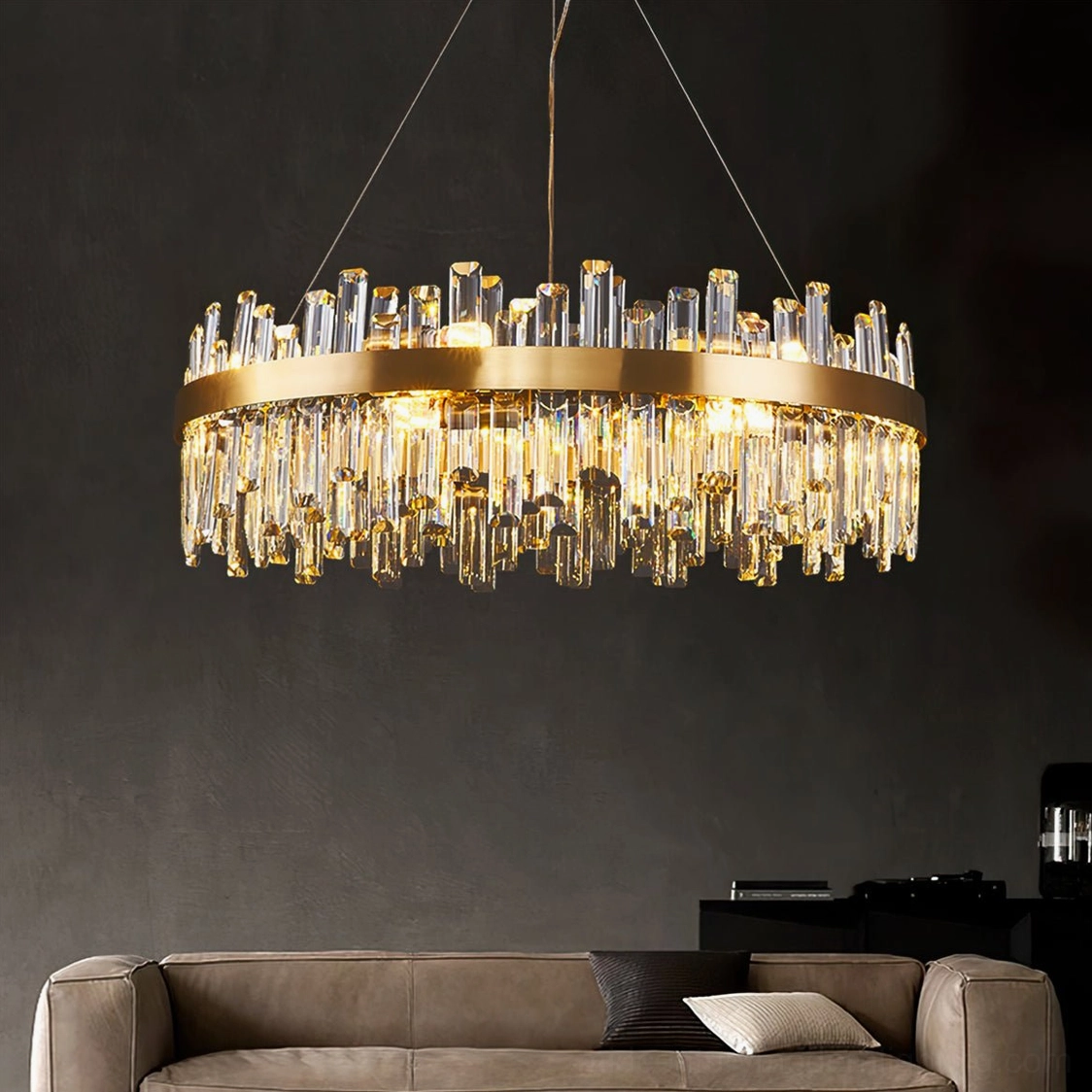 Lit brass crystal chandelier in modern dark living room with tan sofa, warm yellow glowing light through crystals