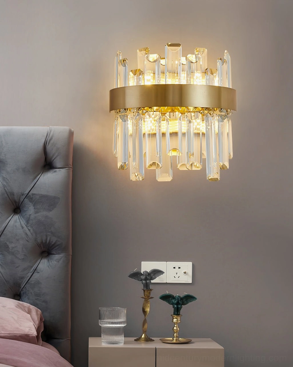 Modern crystal wall fixture paired with tufted gray headboard in master bedroom, providing soft ambient bedside illumination