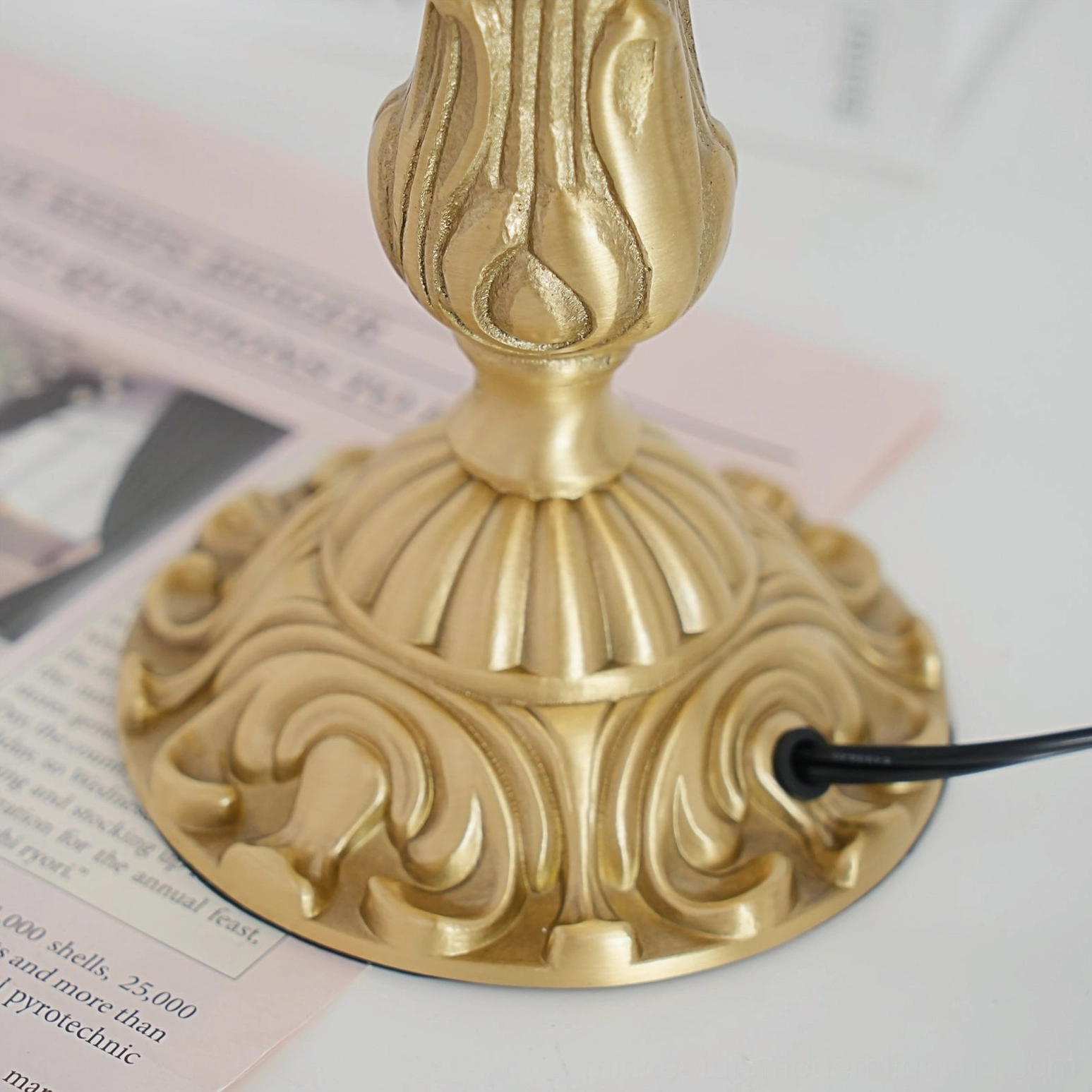 Close-up of intricate carved brass lamp base with black power cord detail