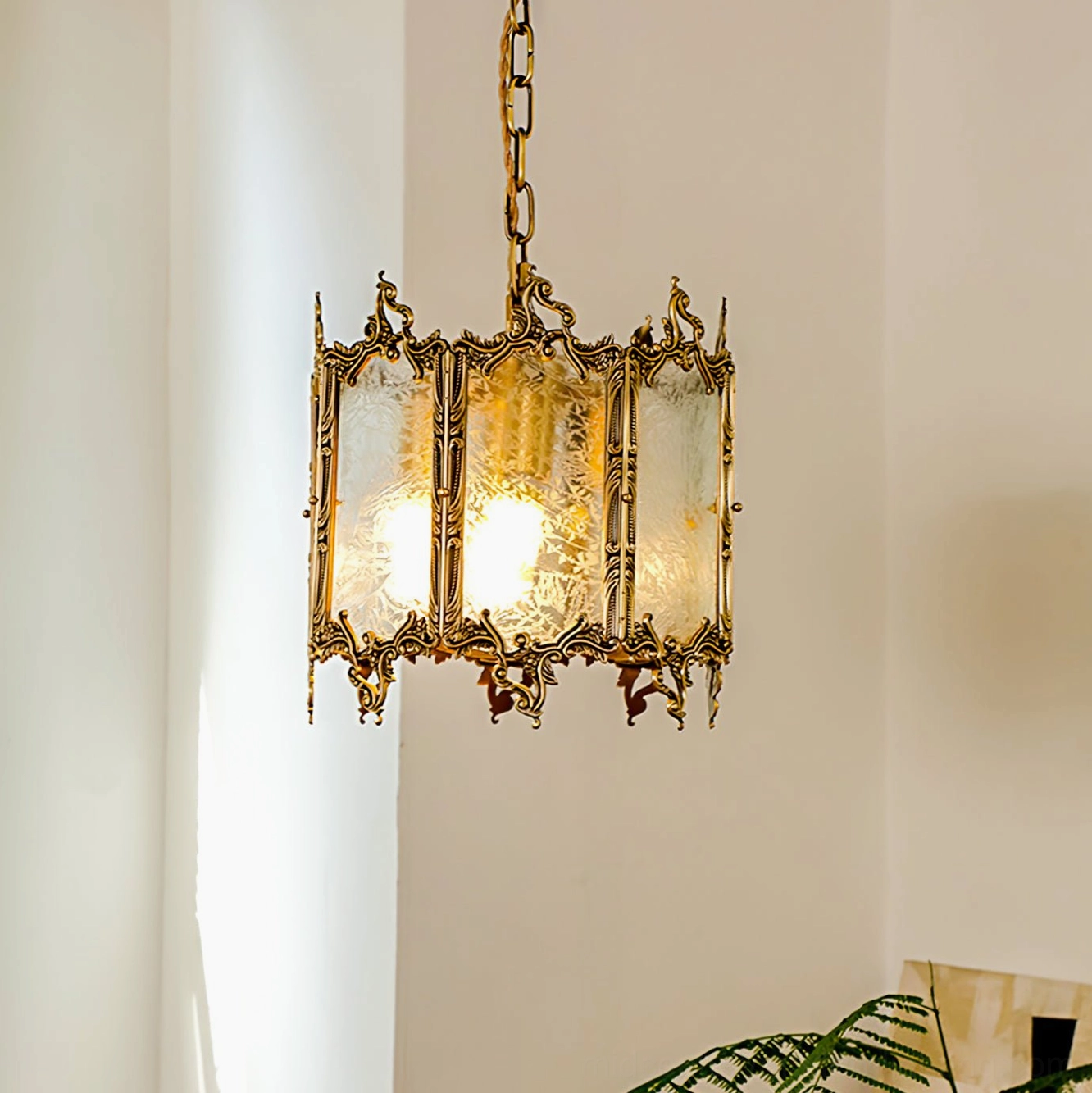 Brass lantern pendant fixture close-up detail showing ornate metal trim, frosted glass construction, and warm glowing light interior