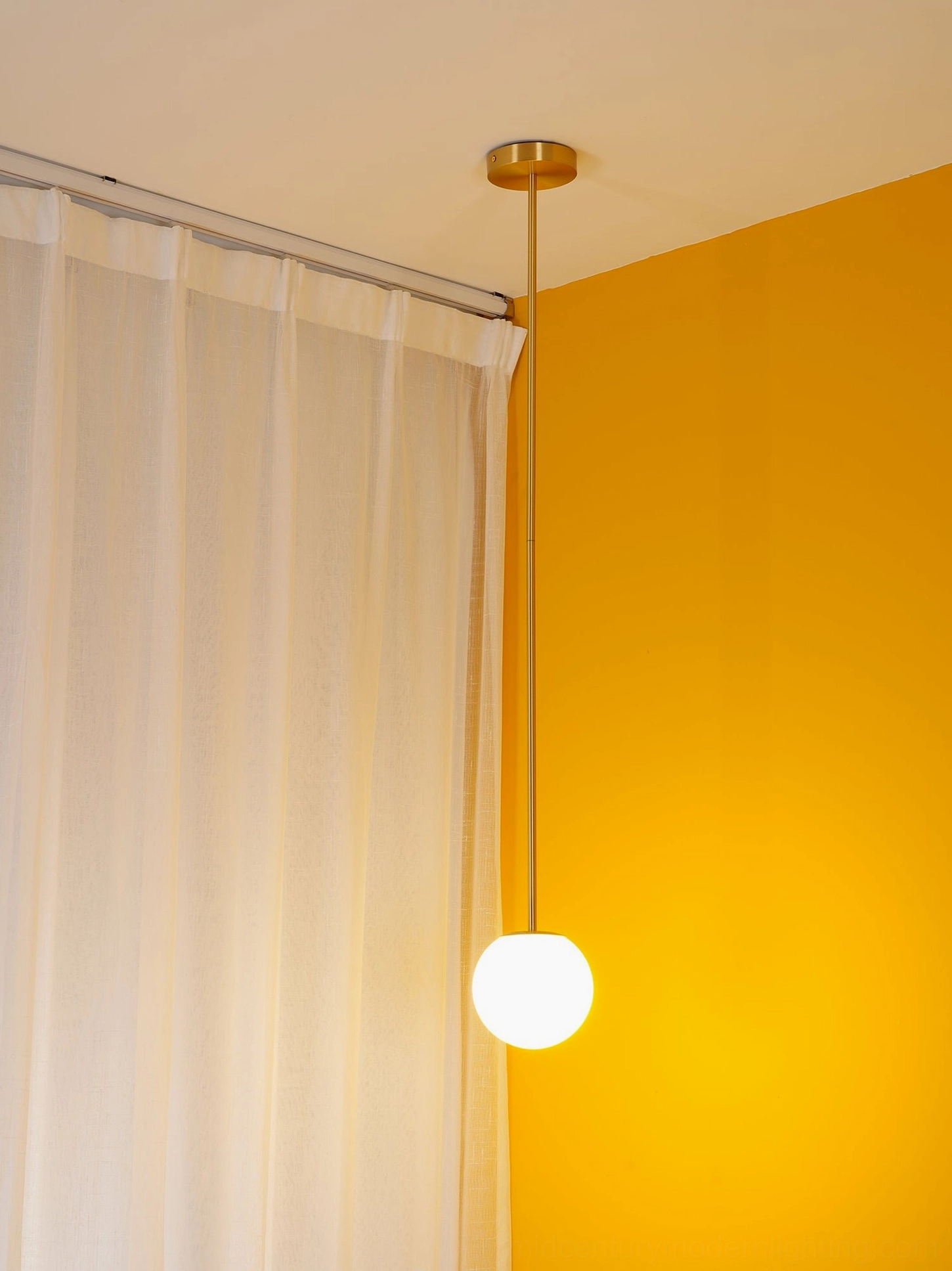 Sleek brass rod pendant light fixture suspended in room with orange wall accent