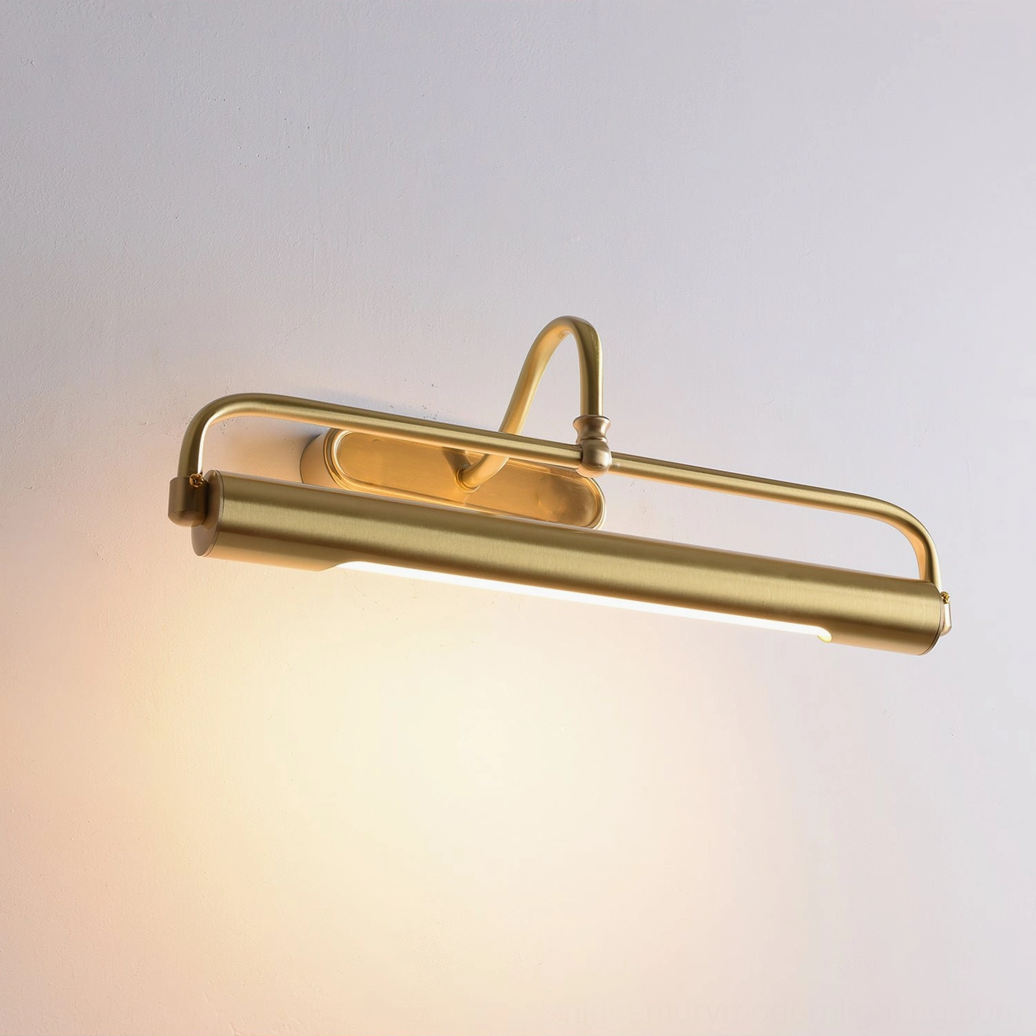 Brass picture light sconce with integrated LED glowing warm, overhead three-quarter perspective