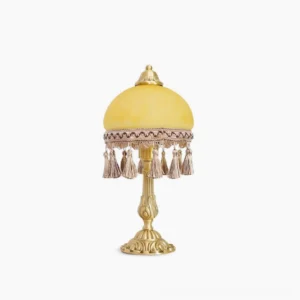 Vintage brass table lamp with yellow frosted glass dome and tassel trim, front view on white background