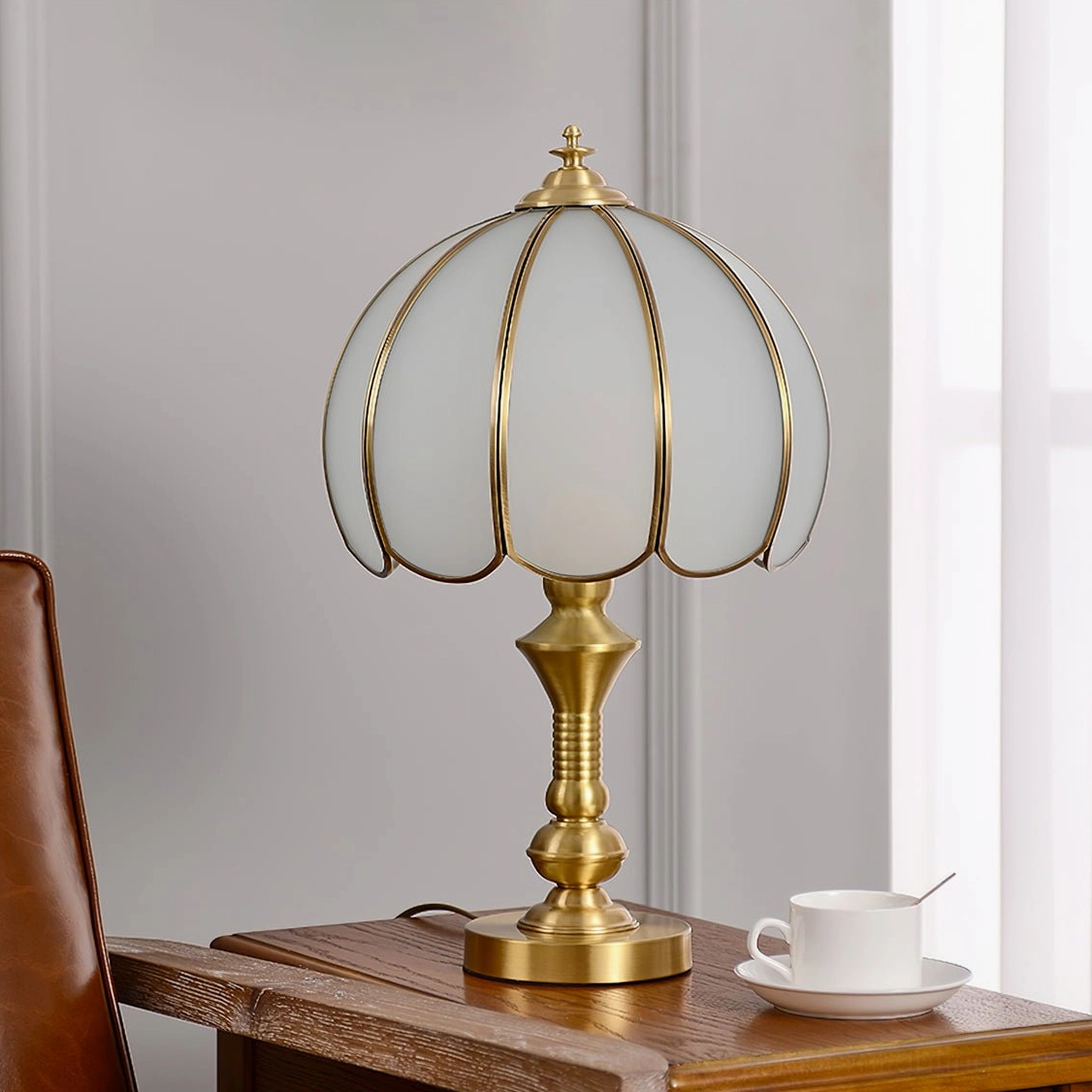 Brass table lamp with ribbed glass shade on wooden side table by window, side view showing warm gold brass finish