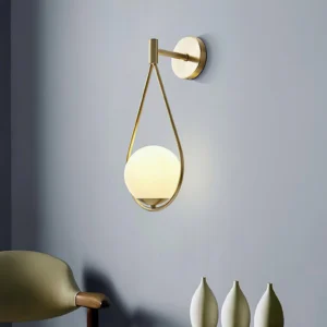Brass wall sconce installed in contemporary living room with grey wall and decorative vases, side perspective showing warm ambient light