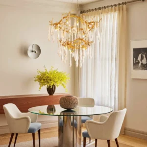 Modern dining room interior featuring brass waterfall chandelier with hanging crystal glass pendants above glass dining table with warm ambient lighting