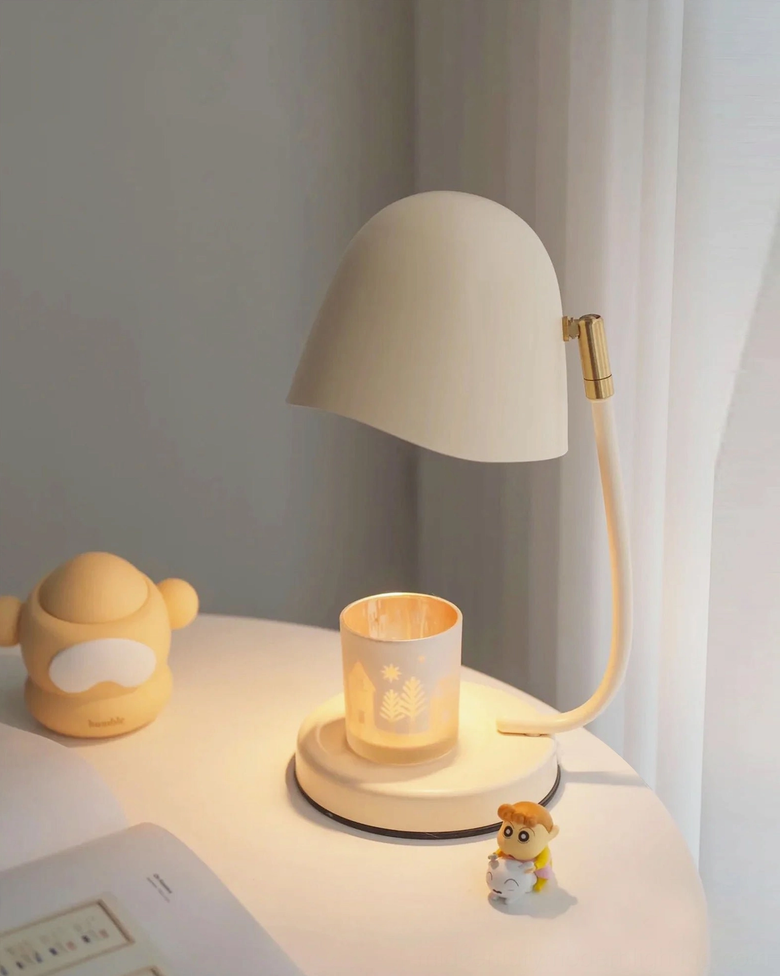 Off-white Breez candlelight lamp on side table with candle holder and decorative figurine, cozy home interior