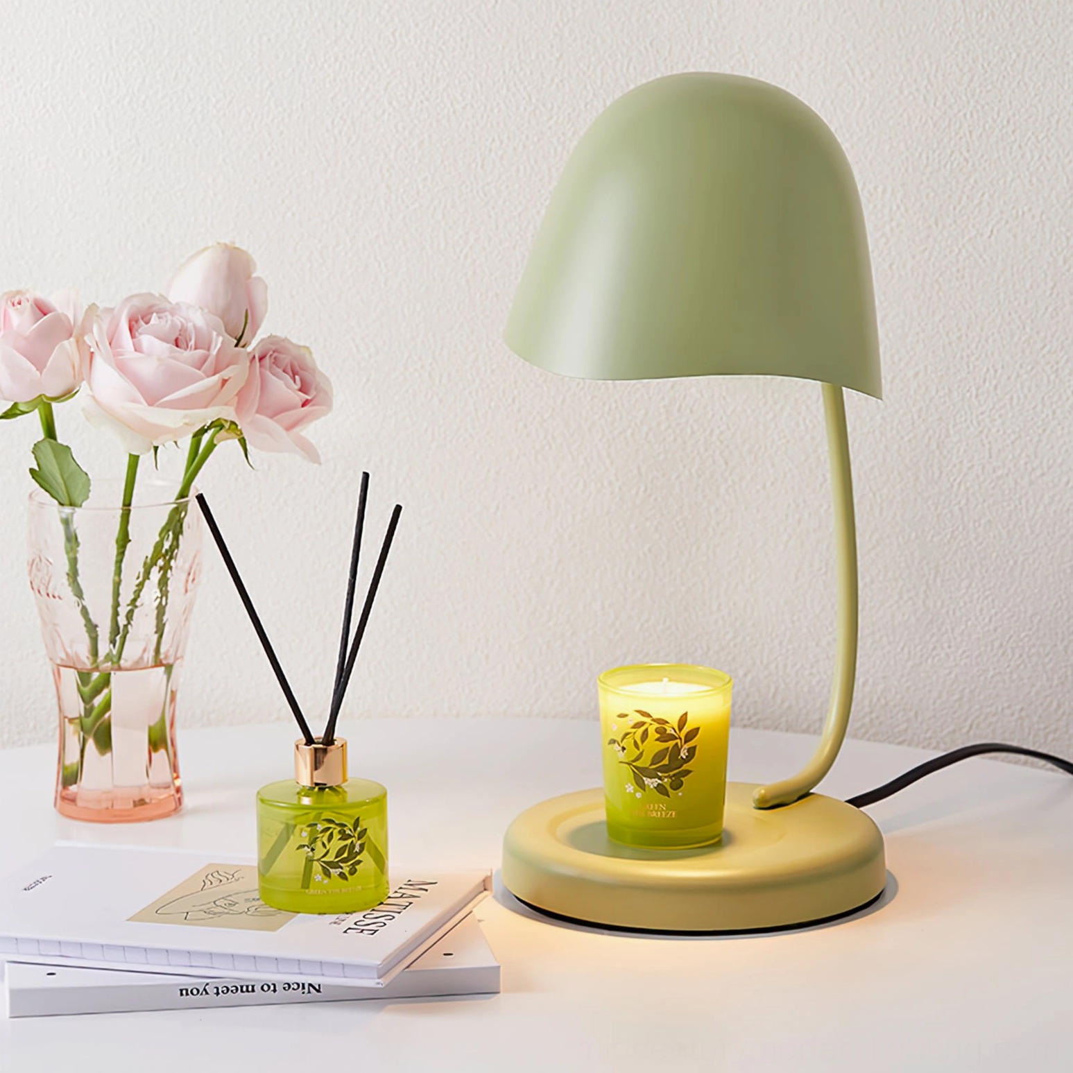 Sage green Breez candle table lamp on minimalist study desk with roses and reed diffuser natural light setting