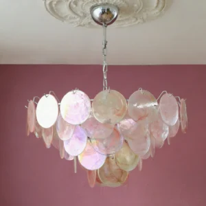 Brette glass disk chandelier installed in elegant dining room with pink accent wall and crown molding creating warm ambient lighting