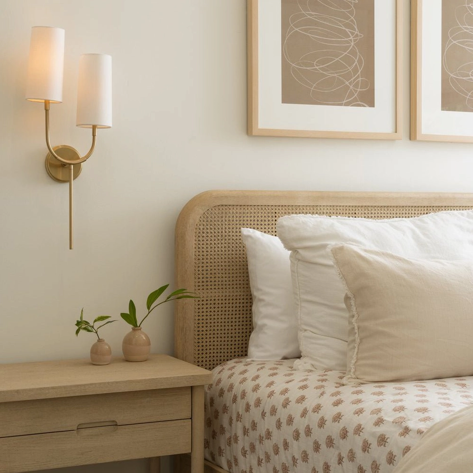 Brio wall sconce in modern bedroom with rattan woven headboard, warm brass finish, side angle view