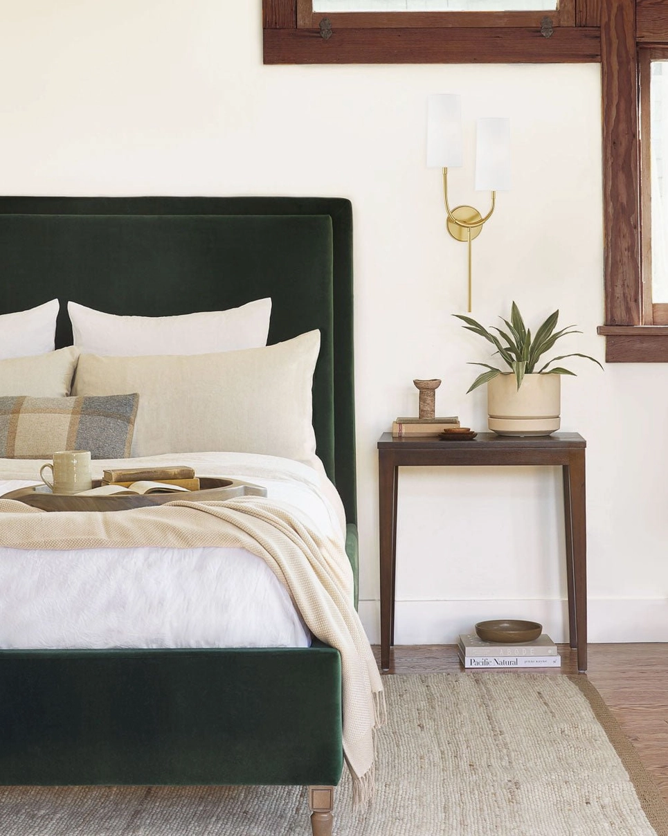 Brio wall sconce accent lighting beside dark green velvet headboard, minimalist brass design bedroom