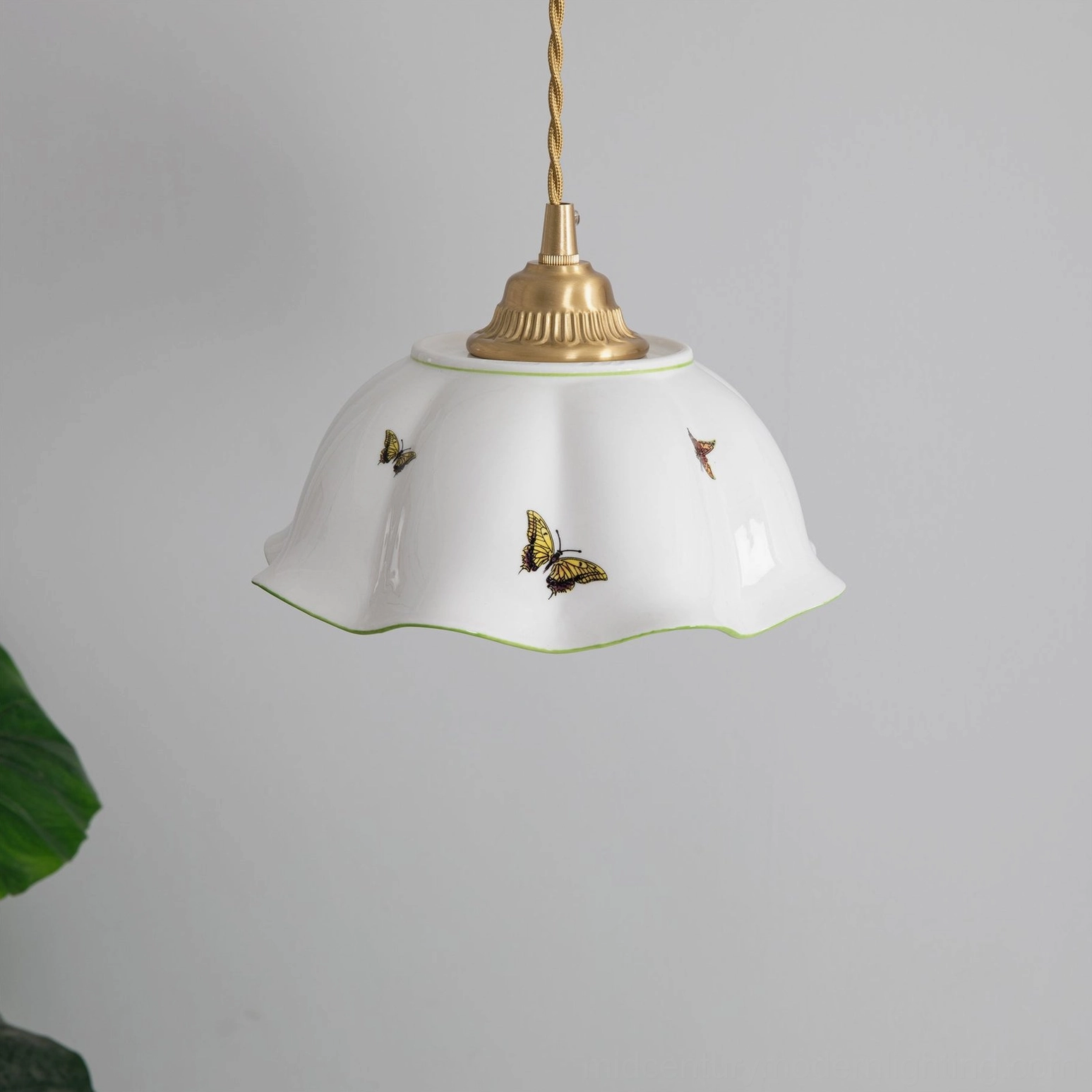 Side view of butterfly ceramic pendant showing twisted hanging cord and detailed butterfly motifs with gray wall backdrop