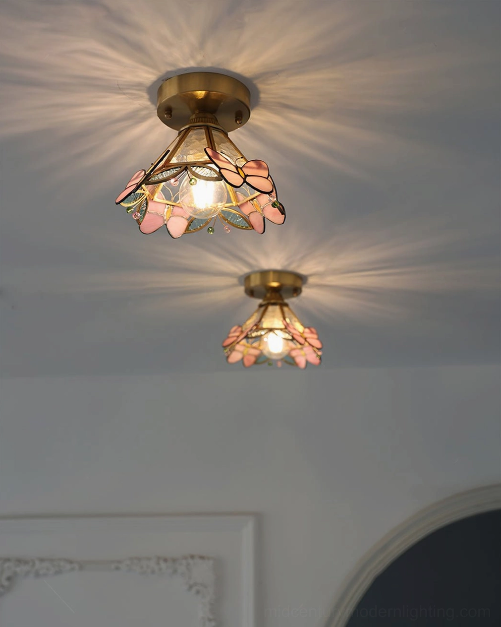 Pair of stained glass butterfly ceiling lights casting warm radial glow from upward angle on gray wall