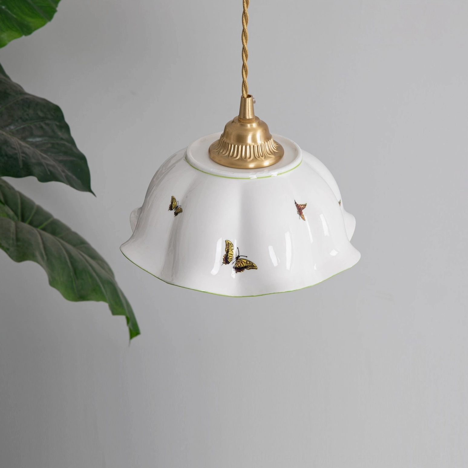 Three-quarter view of illuminated butterfly pendant lamp with brass fixtures displayed in tropical plant setting
