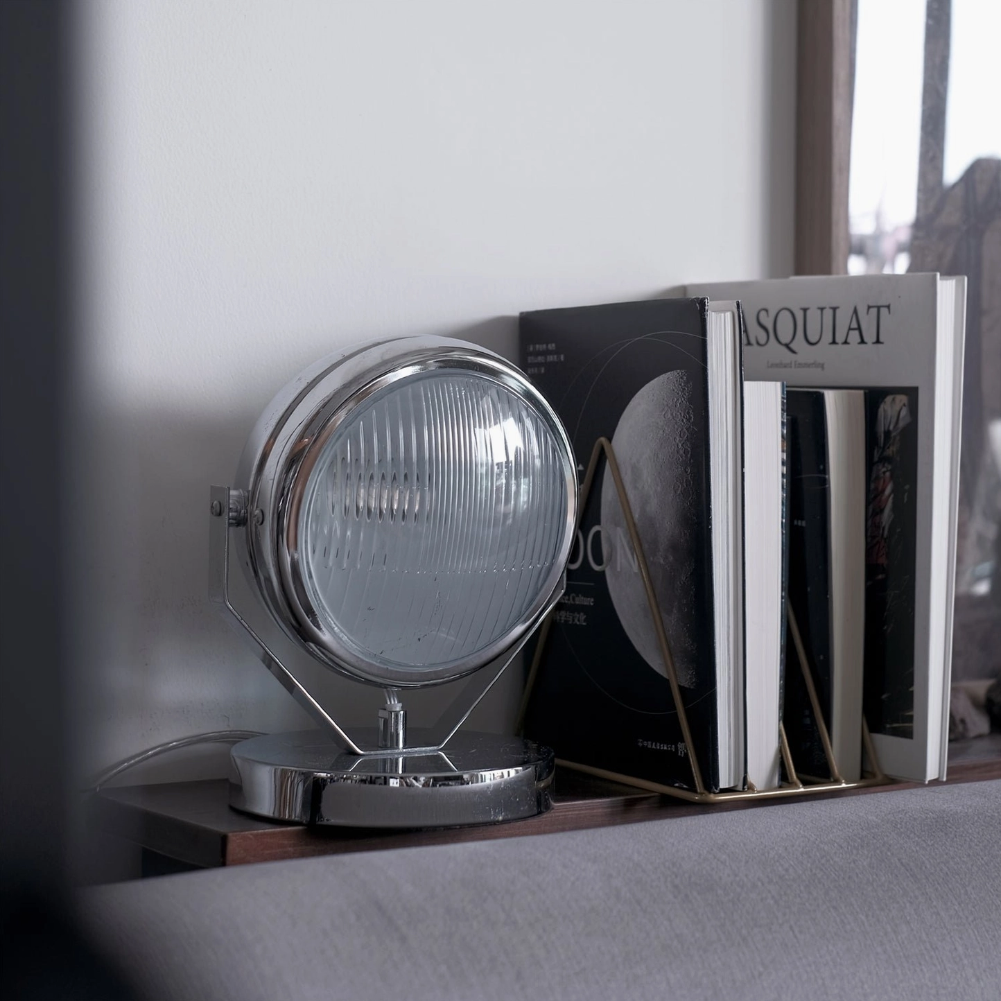 Cadillac chrome table lamp close-up on sofa side table styled with Basquiat art books and minimalist decor