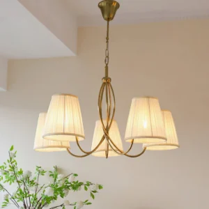 Calistoga brass chandelier illuminated in warm light, low-angle shot showing curved frame and soft glow on cream wall