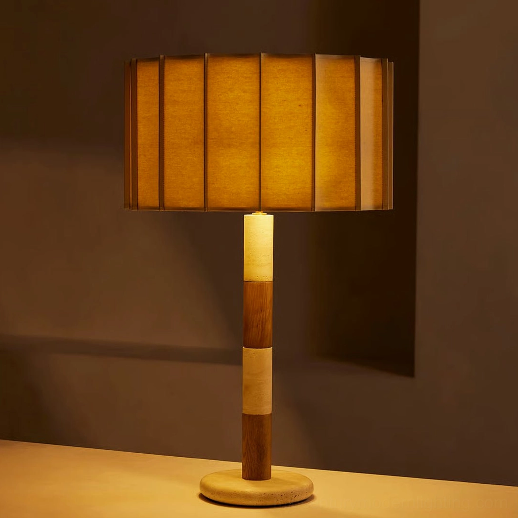 Illuminated Calypso travertine lamp showing warm amber glow through pleated fabric shade with two-tone wooden stem detail