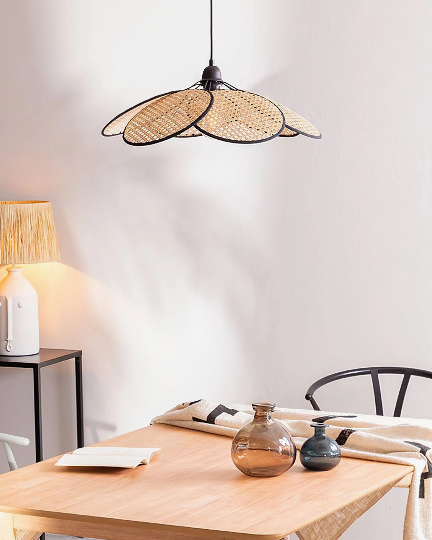 Natural rattan pendant lamp suspended in casual dining area with wooden table, table lamp, and minimalist bohemian home decor styling