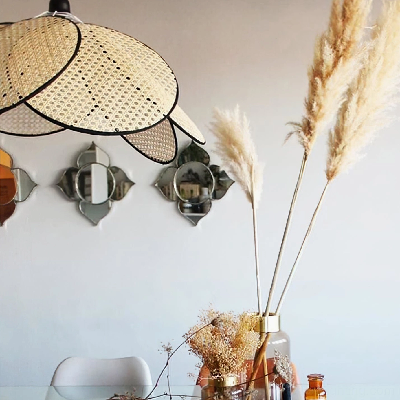 Rattan pendant lamp close-up showing intricate hand-woven petals in rustic bohemian dining wall setting with decorative mirrors and pampas grass