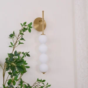 Unlit Candied Haws wall sconce mounted on green foliage wall, side view showing brass hardware and frosted glass spheres