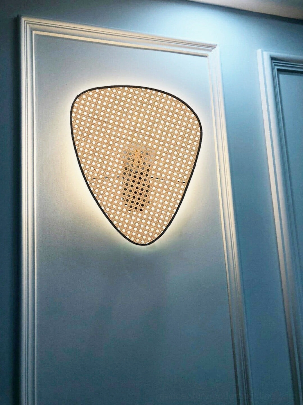 Rattan cannage wall lamp front close-up on blue paneled accent wall showing woven pattern and warm glowing light
