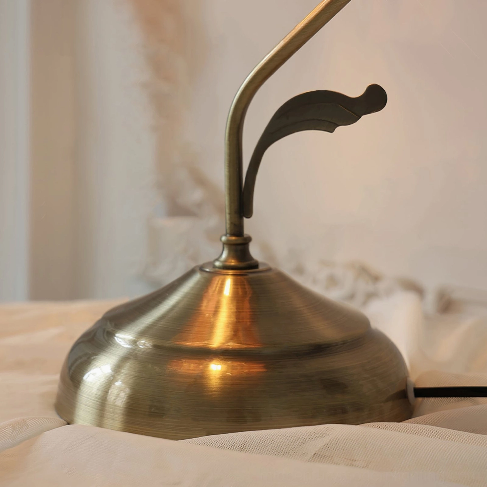 Bronze metal lamp base and curved arm close-up, brushed bronze finish with leaf-shaped metal detail, low side angle on bedding