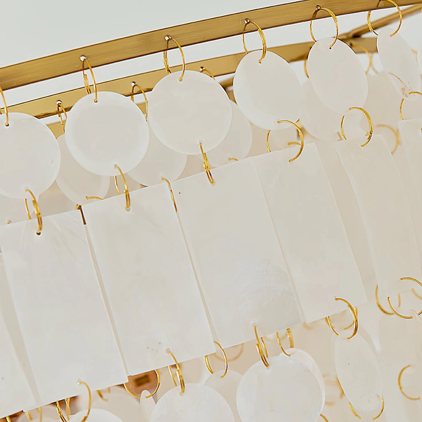 Overhead close-up of capiz shell chandelier component showing individual shells fixed by gold metal rings and brass frame detail