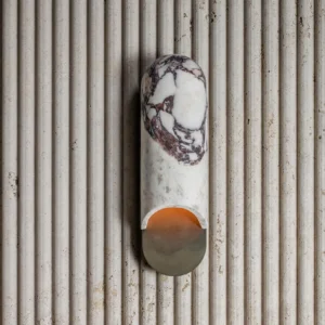 Overhead view of beige travertine capsule wall lamp mounted on fluted accent wall with ambient warm light