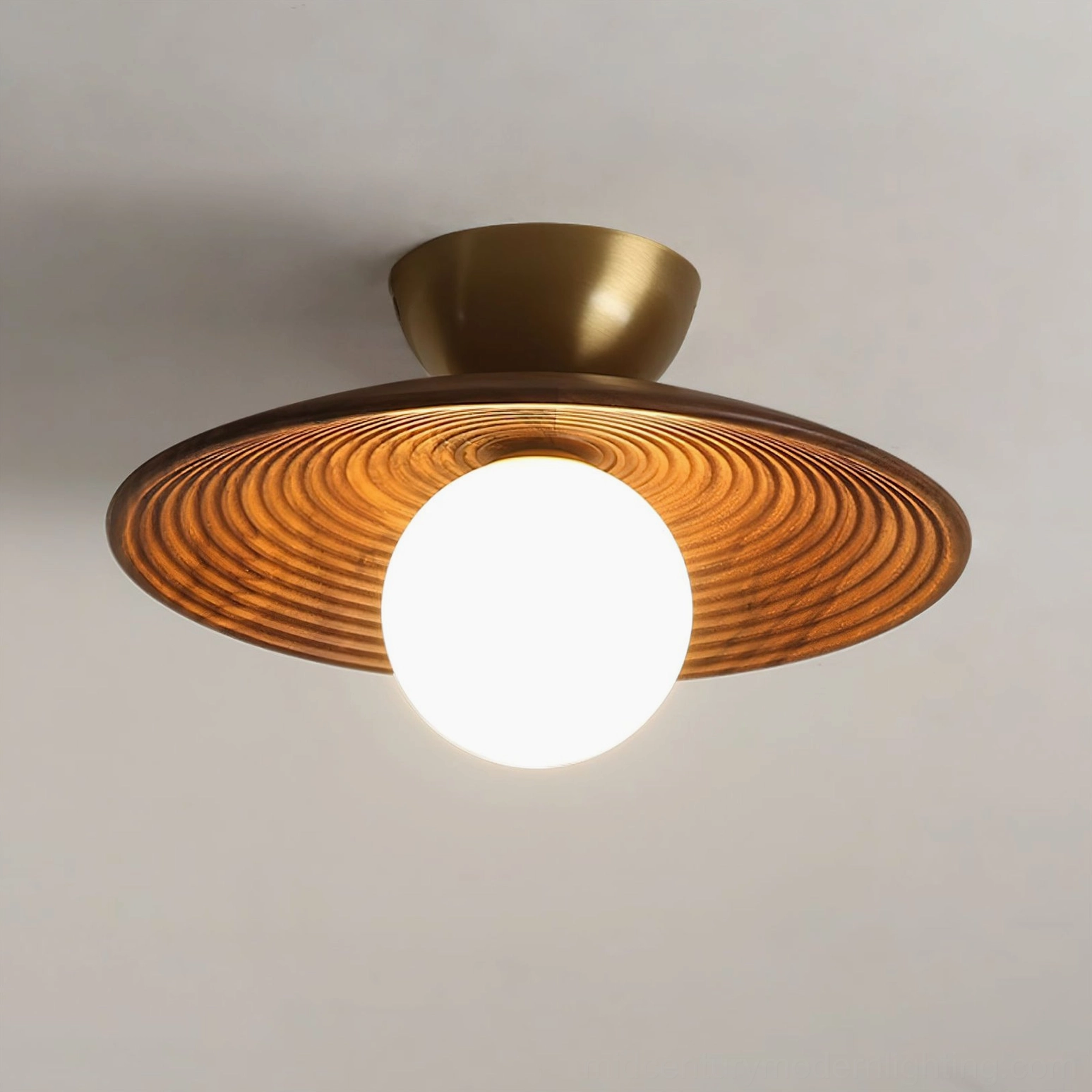 Carapace ceiling light illuminated showing warm ambient glow from frosted globe and brushed gold metal base