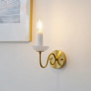 Carlita wall lamp side view with warm lit candle-style bulb, brass scroll arm against gallery wall