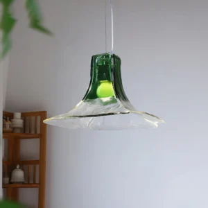 Carlo glass pendant lamp hung in home interior with wooden shelf, green tinted glass shade with warm LED illumination