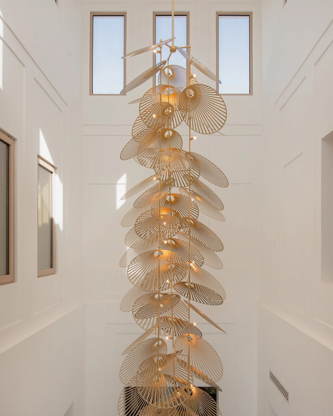 Tall vertical cascade fan chandelier distant view in high-ceiling white duplex living space