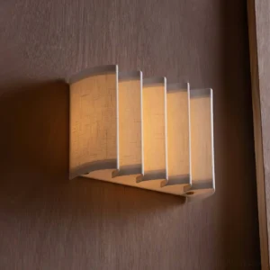 Cascade wall sconce glowing with warm light on dark wood wall panel, side angle close-up