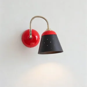 Casper wall sconce mounted on interior wall, red and black finish with warm glowing light, mid-century task lighting