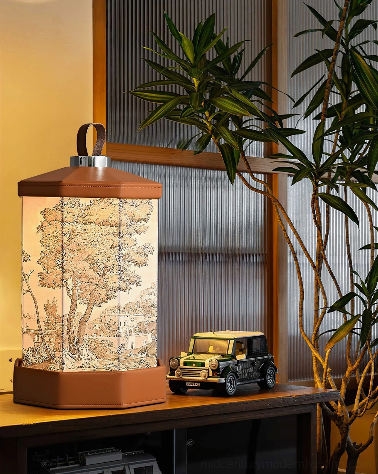 Hexagonal Castle landscape table lamp with built-in battery displayed on living room TV cabinet beside mini toy off-road vehicle and potted green plants, modern interior arrangement