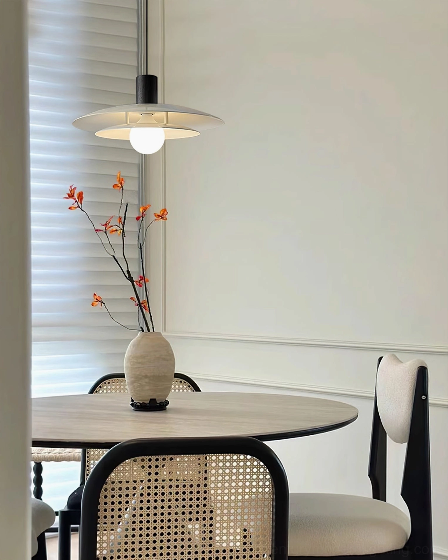 Single pendant fixture with warm wood accents above round casual dining table with dried flower arrangement