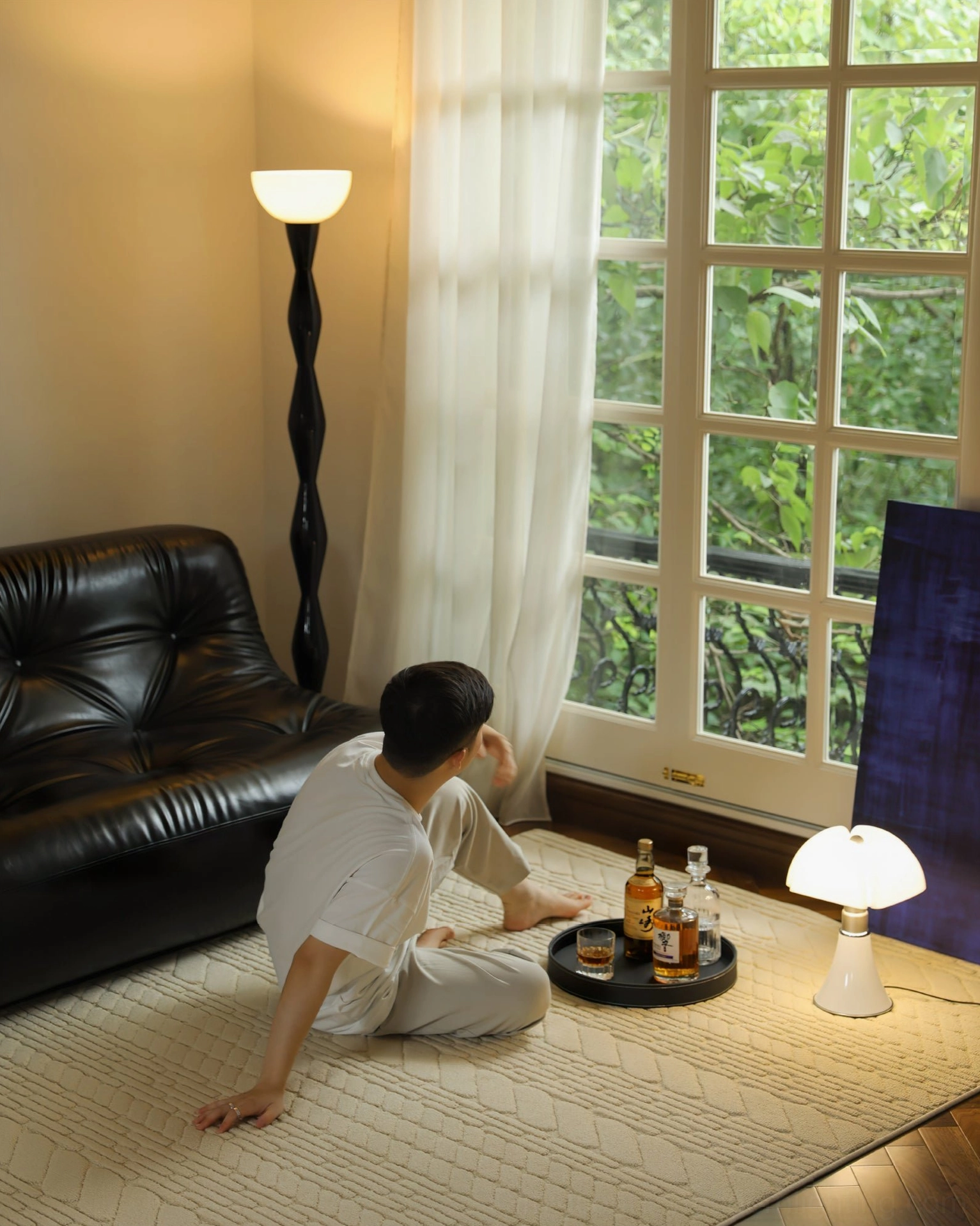 Man sitting on floor beside leather sofa with black torchiere lamp and drink tray in casual home setting