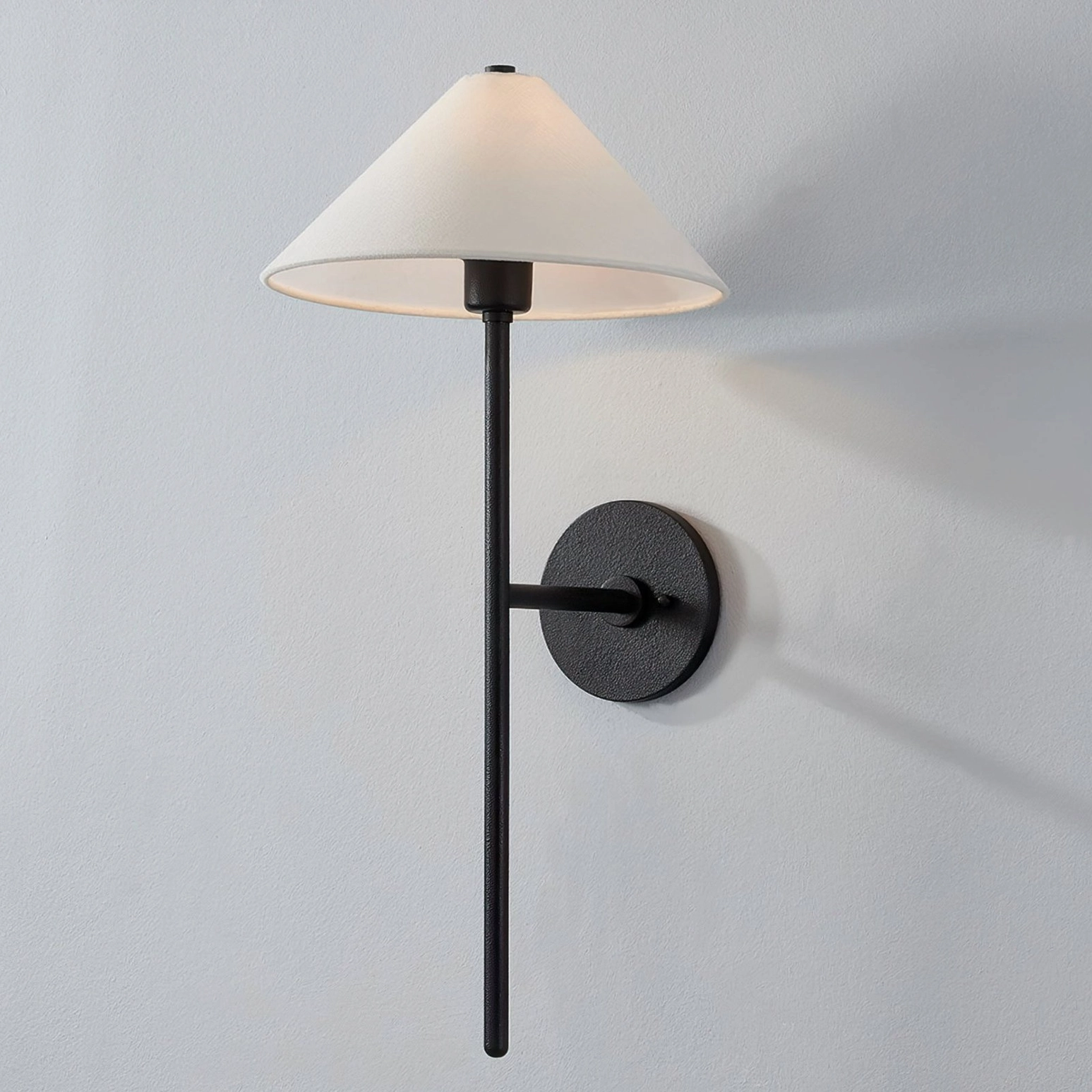 Cedar wall sconce side three-quarter angle showing slim black brass pole and conical fabric diffuser on light gray wall