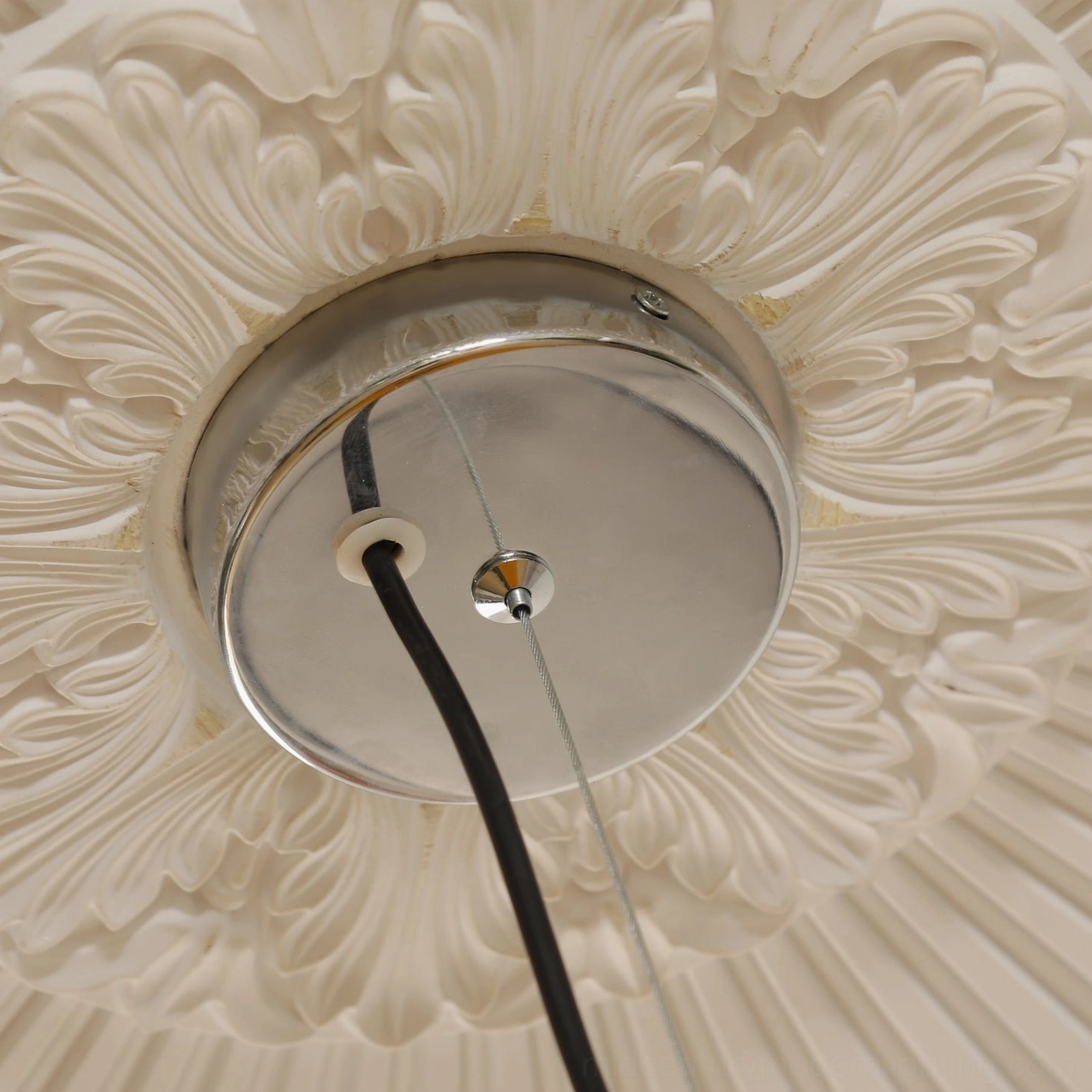 Overhead close-up of pendant light ceiling canopy with polished chrome hardware and black hanging cord on carved ceiling medallion