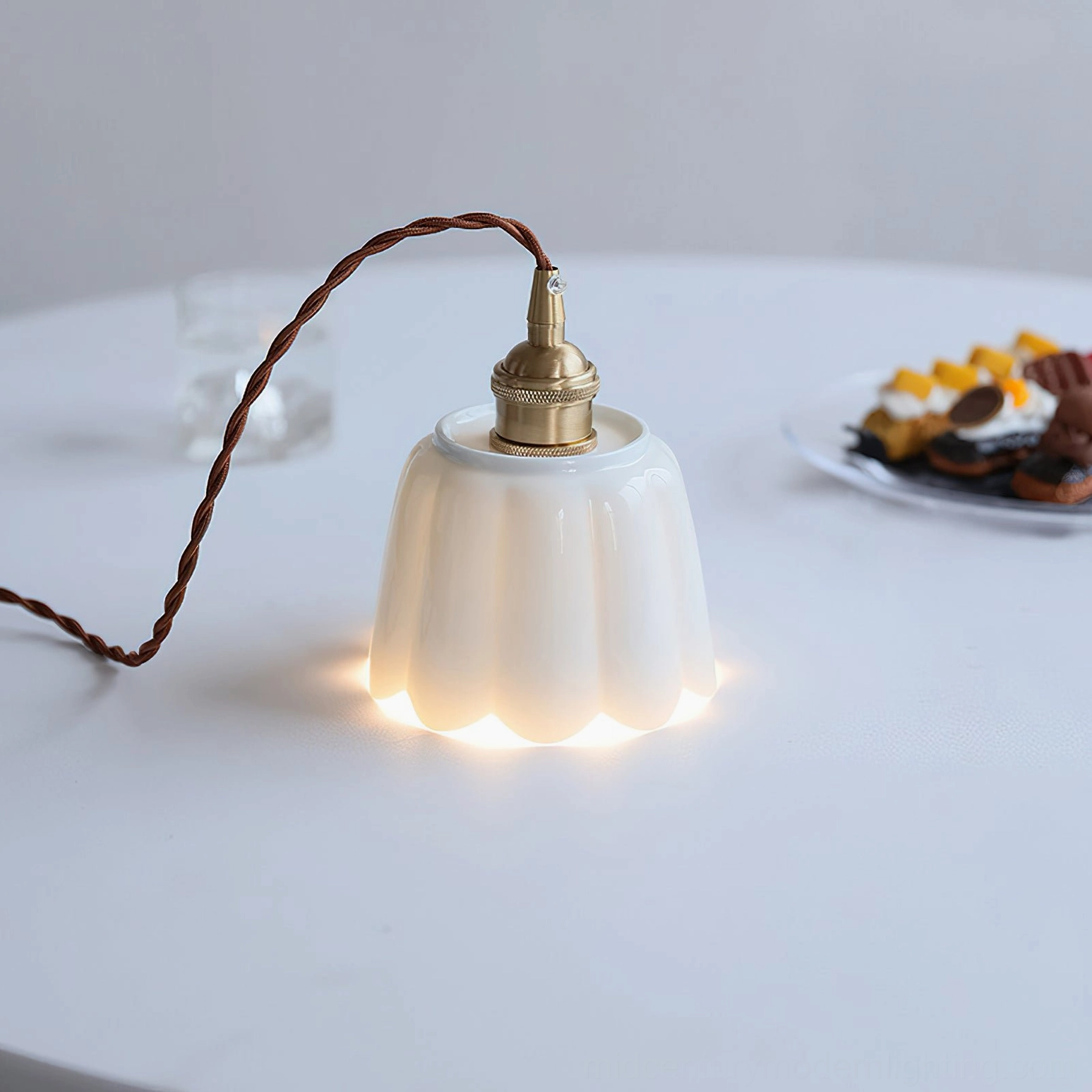 Ceramic pendant light fixture with fluted design glowing above dining table dessert setting