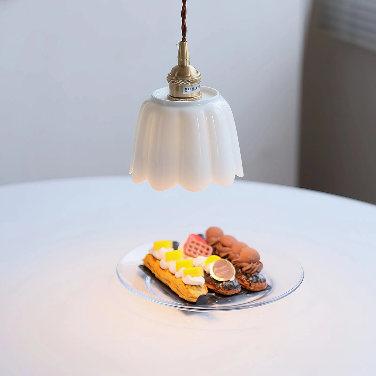 Bright white ceramic fluted pendant with brass hardware positioned above dining table with desserts