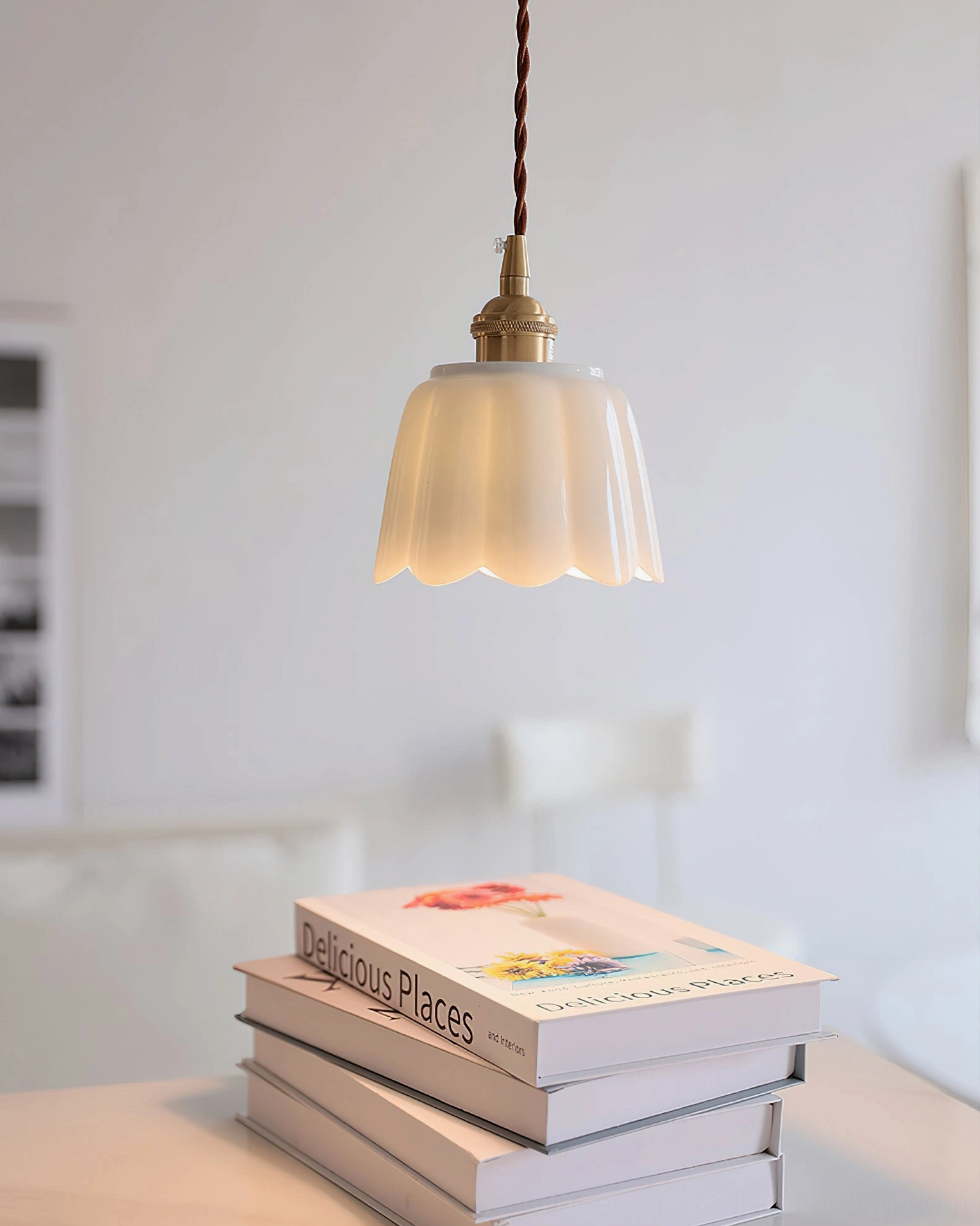 White ceramic fluted pendant with brass fixture suspended above reading corner with stacked books