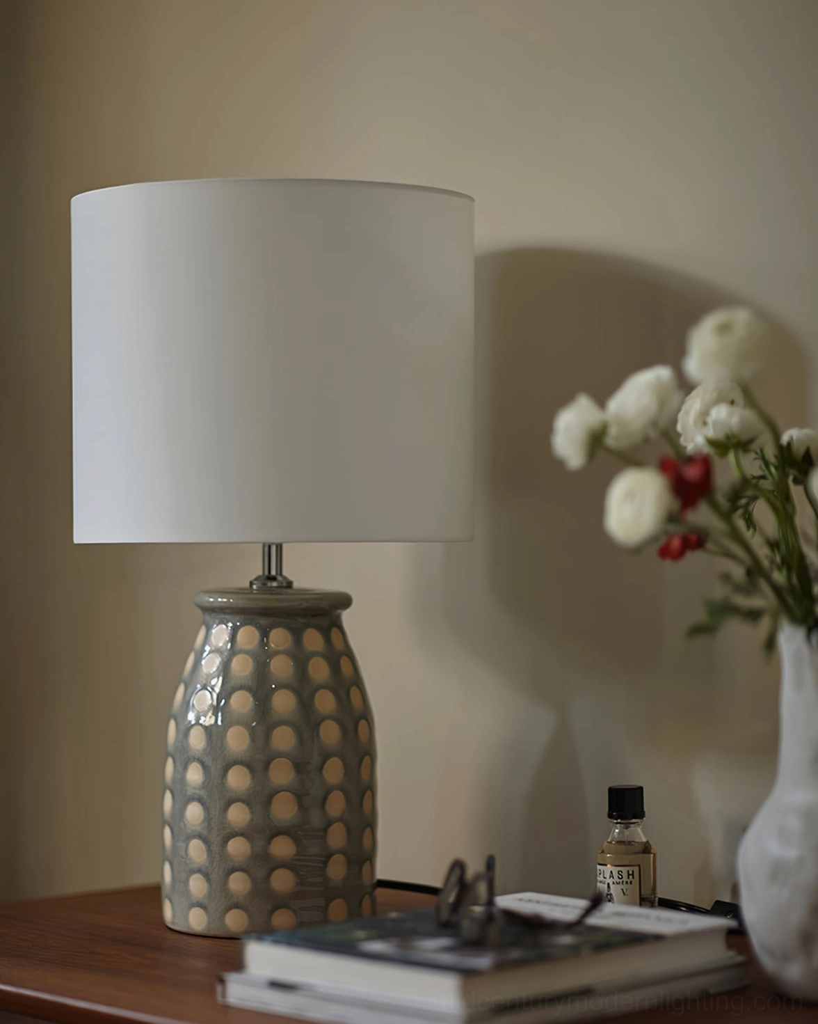 Patterned ceramic table lamp on wooden desk with white vase, stacked books and home accessories, bohemian interior design