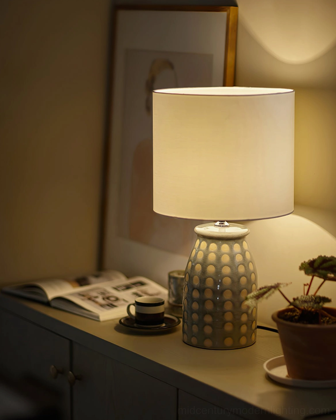 Illuminated ceramic patterned lamp on cabinet desk with magazine, coffee cup and potted plant, contemporary interior