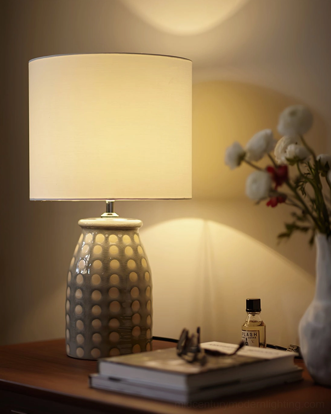 Close-up of lit ceramic patterned lamp on wooden desk with warm wall glow, stacked decorative items and home styling
