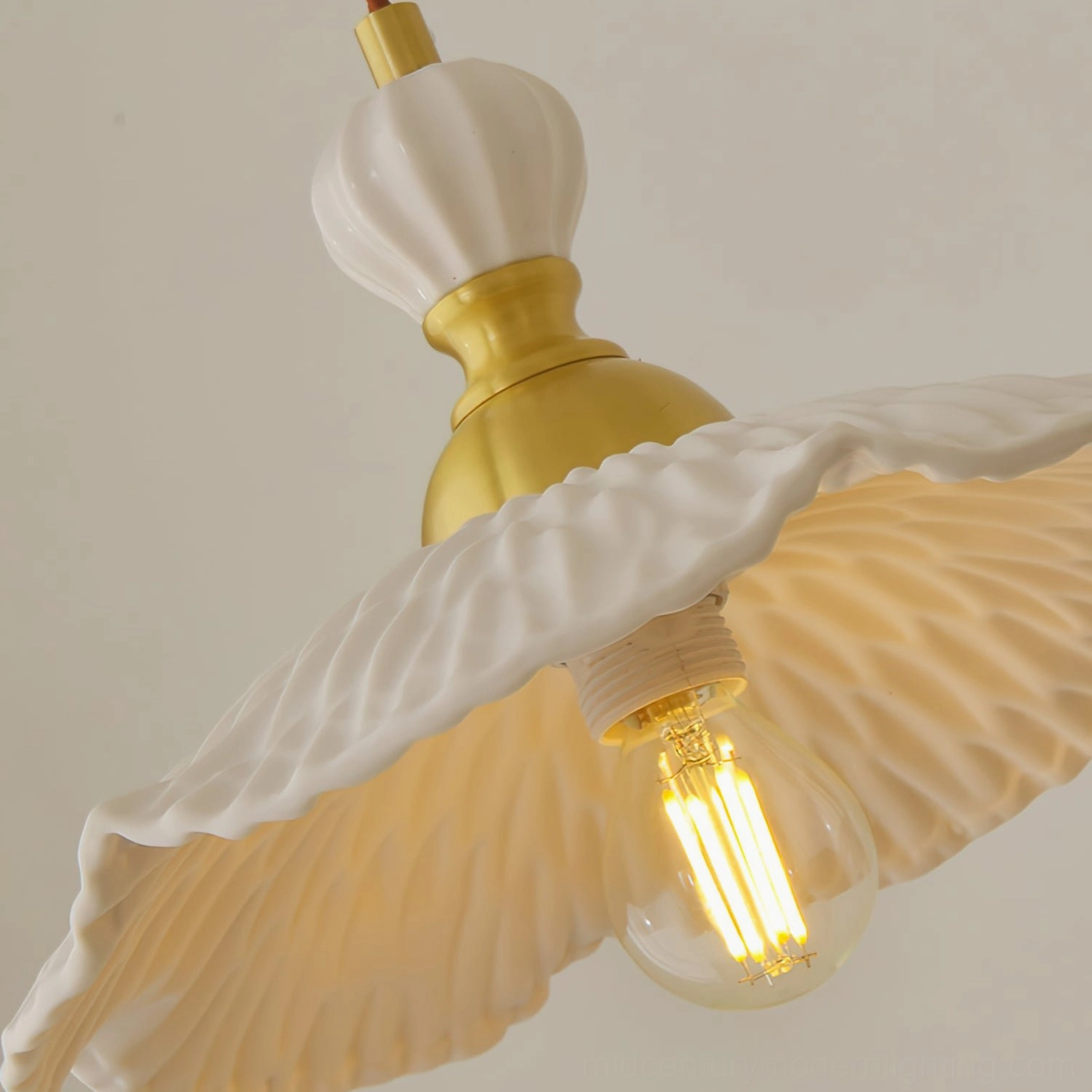 Close-up of ruffled white ceramic pendant shade with exposed Edison bulb and brass mounting hardware