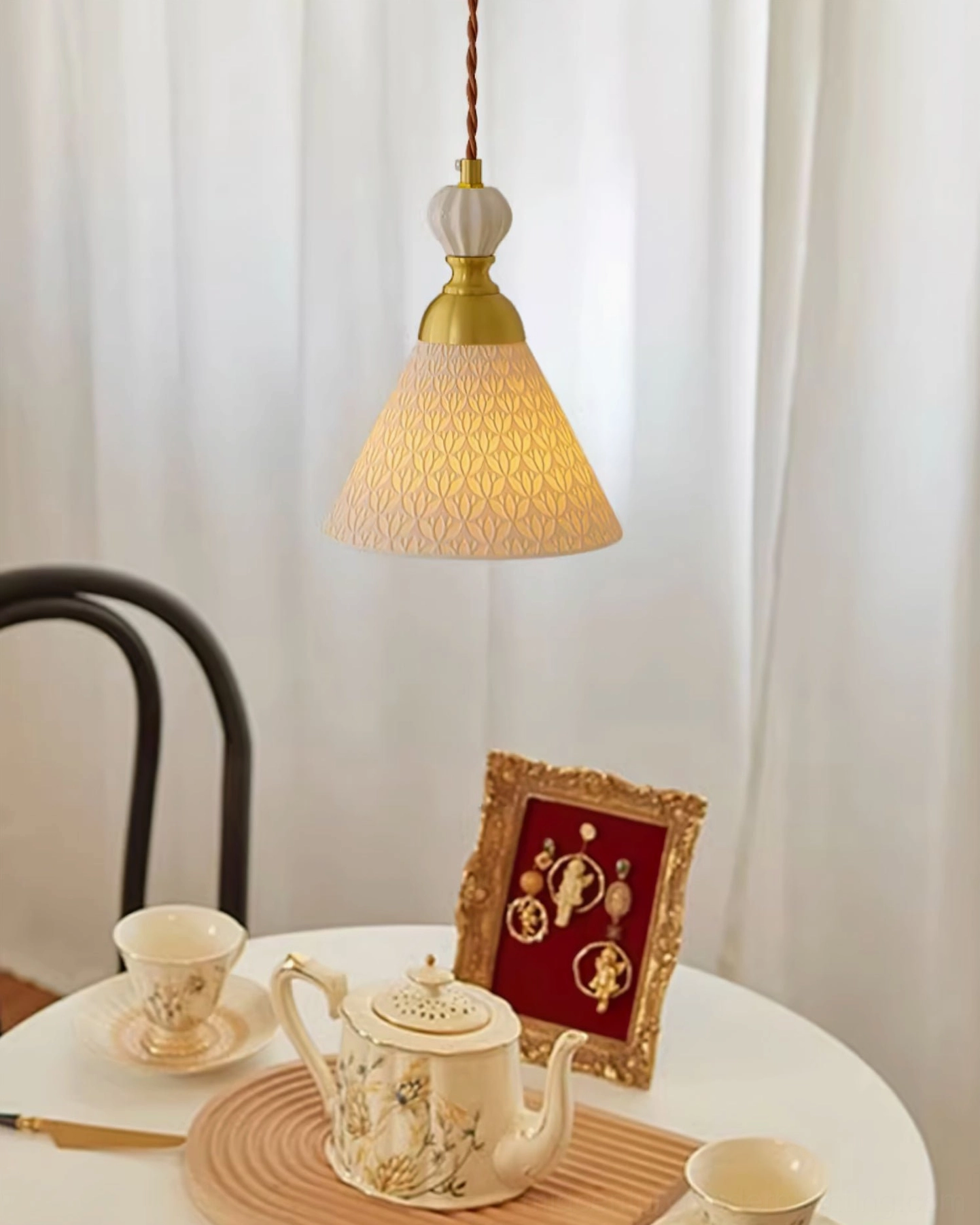 White ceramic pendant with brass cap hanging above dining table with tableware and warm ambient lighting