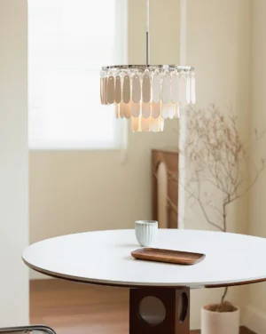 Modern tiered pendant chandelier illuminated in minimalist dining room with round white table
